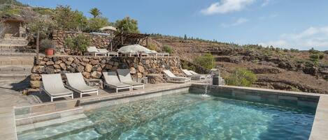 A clear swimming pool with lounge chairs and a stone wall.