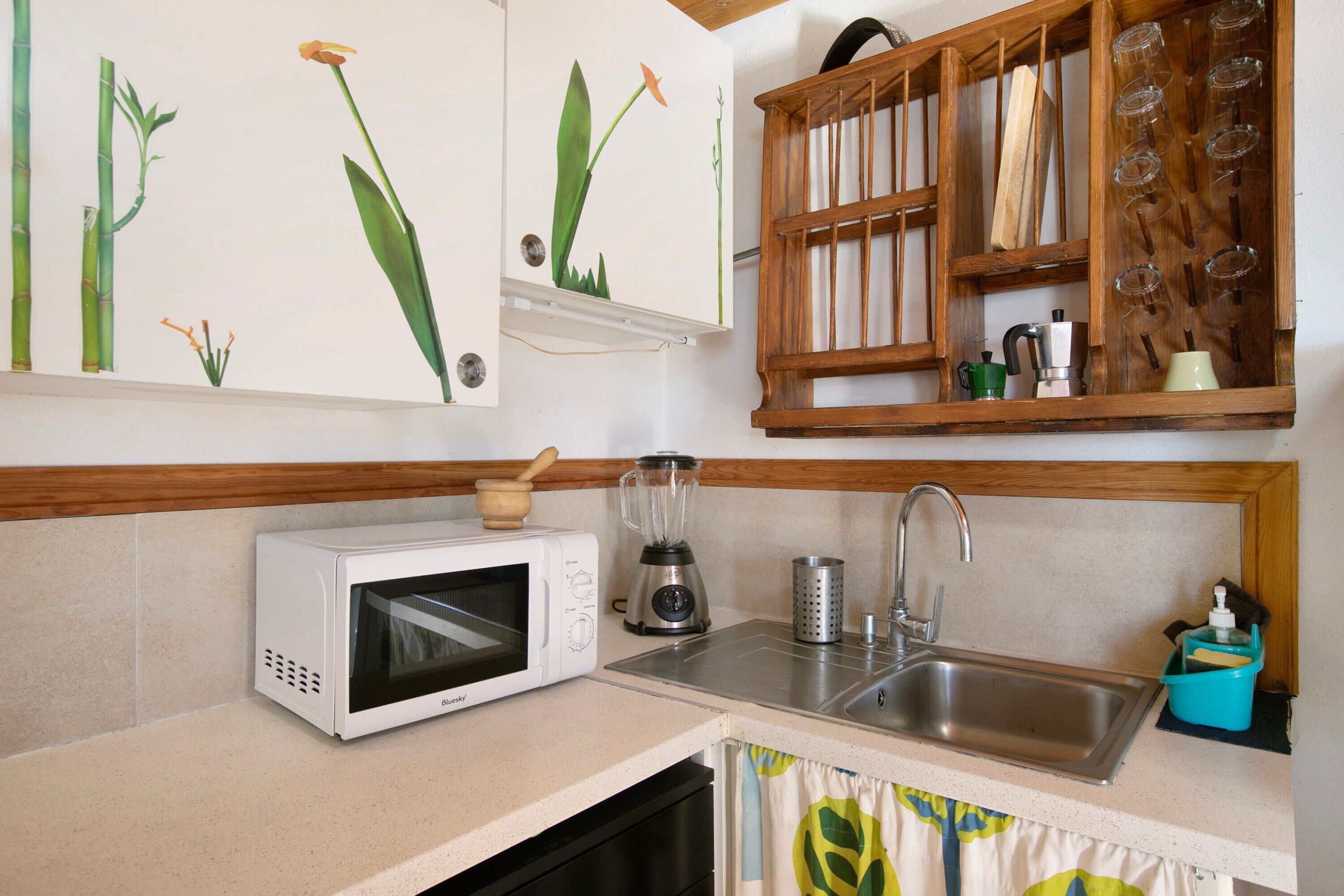 Una cucina con forno a microonde, frullatore, lavello e scaffali in legno con bicchieri.