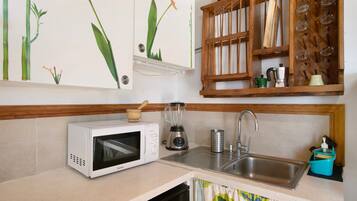 Una cucina con forno a microonde, frullatore, lavello e scaffali in legno con bicchieri.