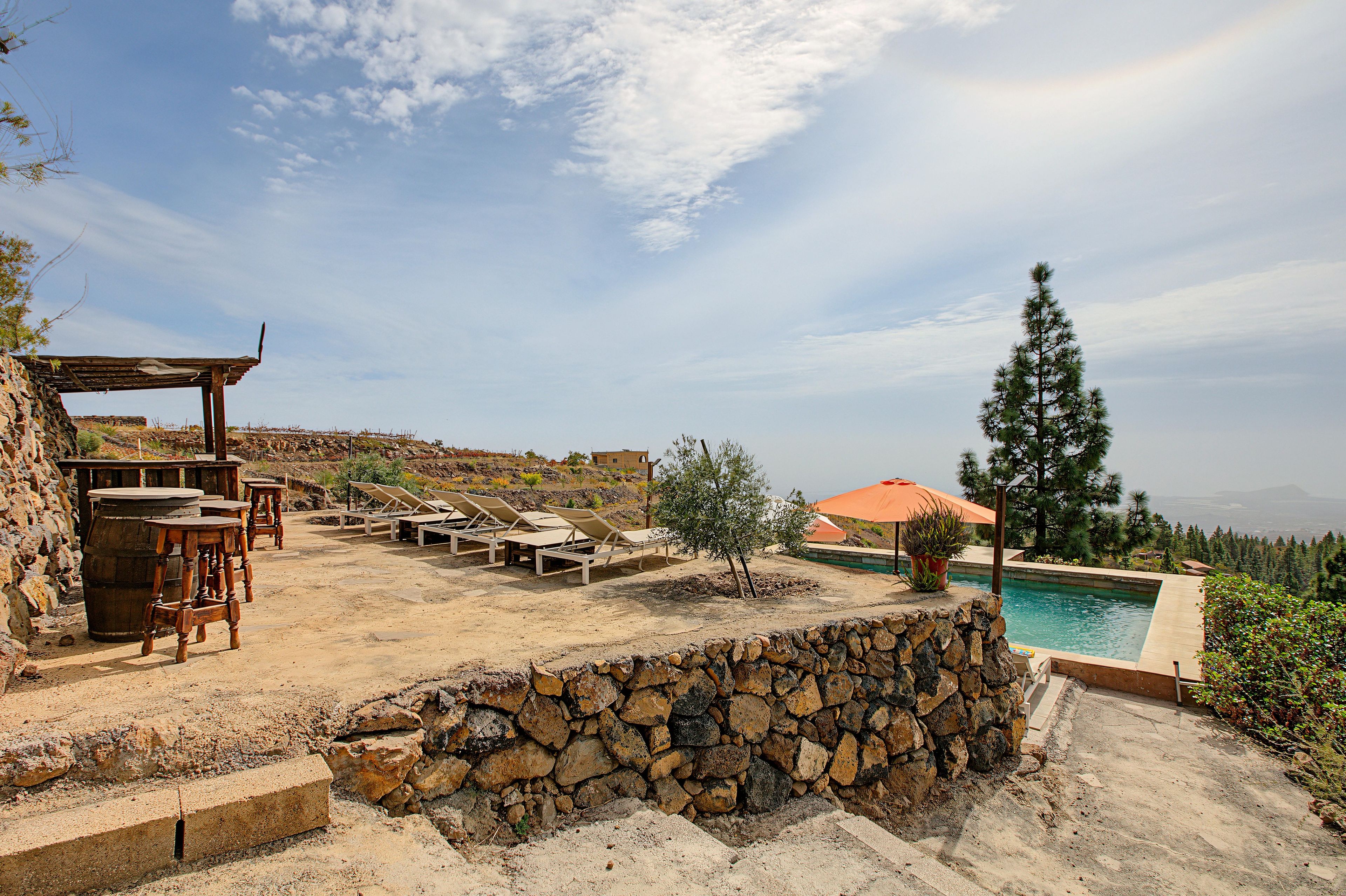 Zona de piscina con sillas de descanso, una pérgola y vistas al paisaje.