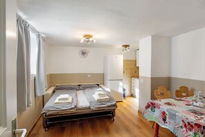 Une pièce de taille modeste comprenant un lit, un petit coin cuisine, une table à manger avec une nappe et une horloge au mur.