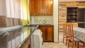 Een keuken met houten kastjes, een fornuis, een wasmachine en een eethoek met stoelen en een tafel.