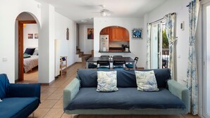Una sala de estar con un sofá, una mesa de comedor con sillas, una zona de cocina y una escalera que lleva a otra habitación.