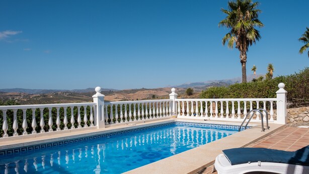 Una piscina con barandilla blanca, una silla de descanso y vistas a colinas distantes.