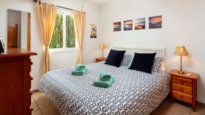 Un dormitorio con una colcha estampada, dos lámparas de noche, una mesita de noche de madera, un espejo y una ventana con cortinas.