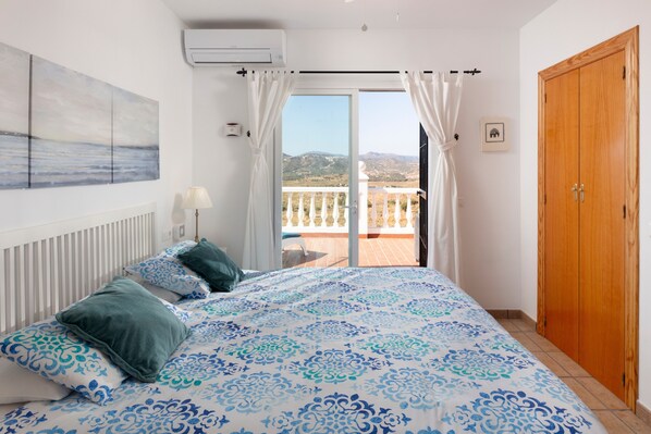 Un dormitorio con cama, vistas al exterior, una puerta de madera y un ventilador de techo.