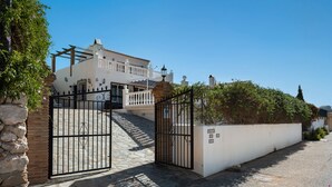 Una entrada con portón a un edificio, con un sendero de piedra que conduce a un edificio blanco con balcón.
