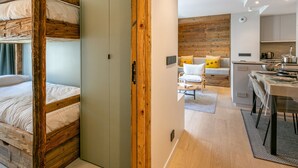 Una habitación moderna con literas, un armario de madera, una kitchenette y un área de descanso con cojines.