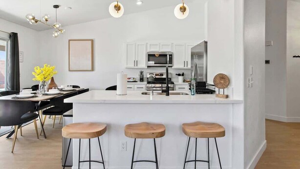 A modern kitchen with white cabinets, a central island with stools, and pendant lighting. - Lavish 4BR Vegas Pool House w/ Heated Pool + Spa (North Las Vegas)