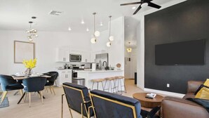 A modern kitchen with white cabinets, a central island, and a flat-screen TV mounted on the wall. - Lavish 4BR Vegas Pool House w/ Heated Pool + Spa (North Las Vegas)