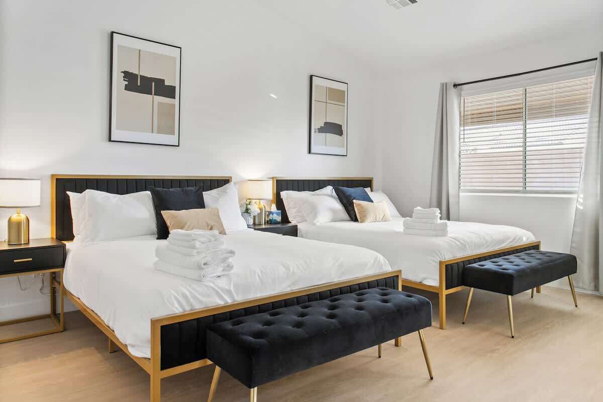 Hotelkamer met twee bedden, een zwarte bank, een nachtkastje met lamp en een raam met zonwering.