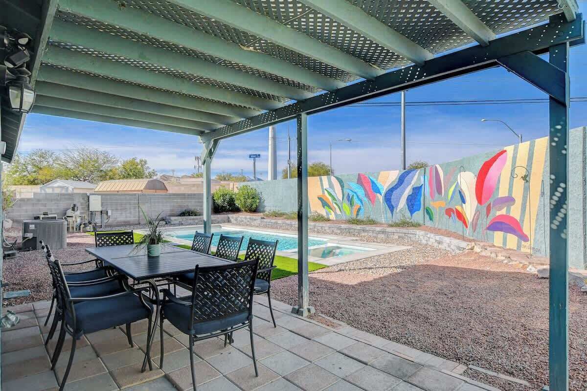 Un patio cubierto con piscina, mobiliario exterior y un colorido mural de fondo.