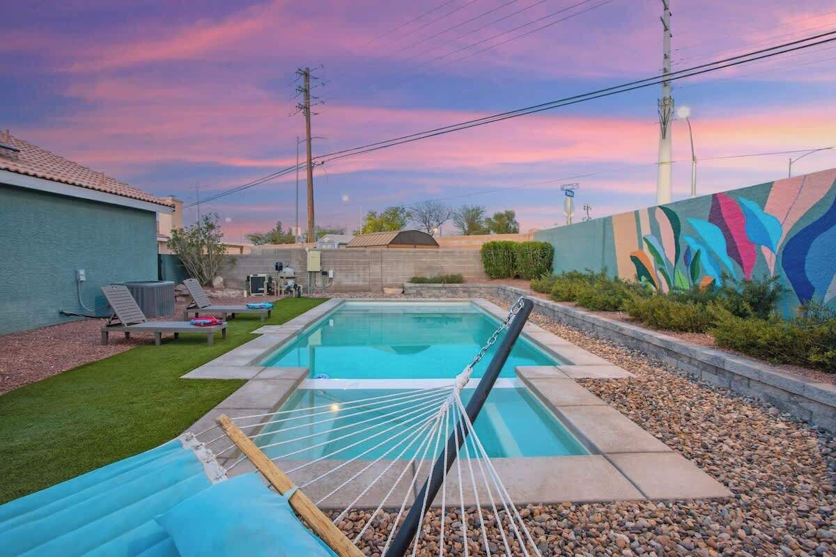 Una piscina con una hamaca, sillas de descanso y un mural en la pared.