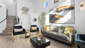 A modern living room with a staircase, a large painting, and a chandelier. - Vegas 5BR: Movie Theater, Pool, Hot Tub & Arcade (North Las Vegas)