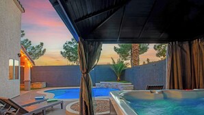 A covered outdoor area with a hot tub, lounge chairs, and a swimming pool. - Vegas 5BR: Movie Theater, Pool, Hot Tub & Arcade (North Las Vegas)