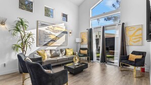 A spacious living room with a large window, a modern sofa, and a coffee table. - Vegas 5BR: Movie Theater, Pool, Hot Tub & Arcade (North Las Vegas)