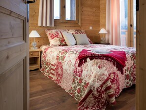 A wooden room with a bed, two bedside lamps, and a window with curtains. - Charming duplex with fireplace and wifi in Courchevel (Courchevel 1550)