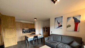 Ein moderner Wohnraum mit grauem Sofa, einem Esstisch mit Stühlen, einer Küchenzeile mit Holzschränken und zwei an der Wand hängenden Bildern.