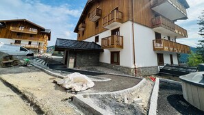 Ein mehrstöckiges Holzgebäude mit Balkonen, einem Steinfundament und einer gepflasterten Fläche mit Baumaterialien.