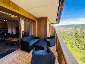 A wooden deck with outdoor furniture, a sliding glass door leading to an interior dining area, and a scenic view of a village and mountains. - New 3-room apartment in Les Saisies, 6 people, parking included (Les Saisies)