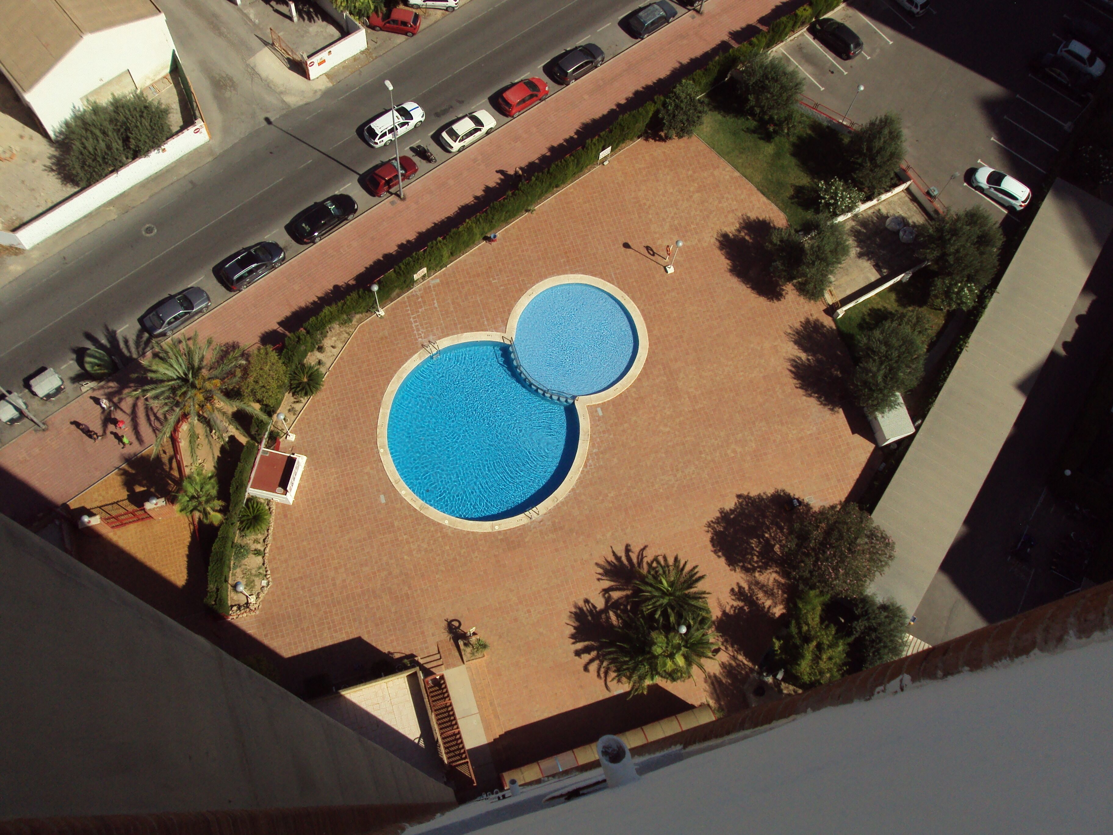 Ein Luftbild eines Poolkomplexes mit zwei großen Pools, umgeben von Palmen und einem Parkplatz.