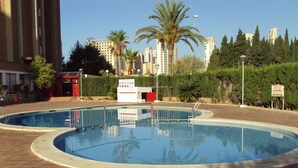 A swimming pool with a tiled deck, surrounded by palm trees and a building in the background. - Stunning 1 bedroom apartment with clear views across Benidorm (Benidorm)
