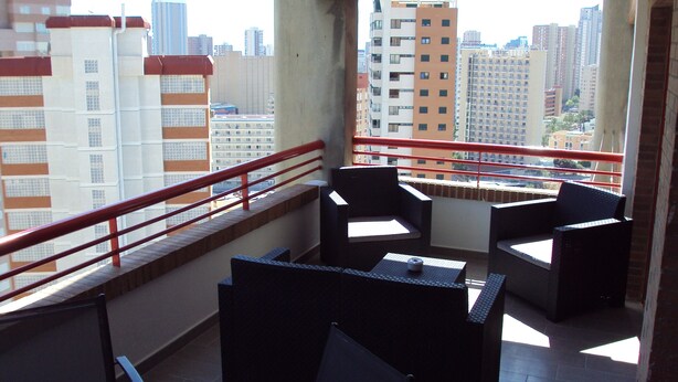 A balcony with a view of tall buildings, a red railing, and black furniture. - Stunning 1 bedroom apartment with clear views across Benidorm (Benidorm)