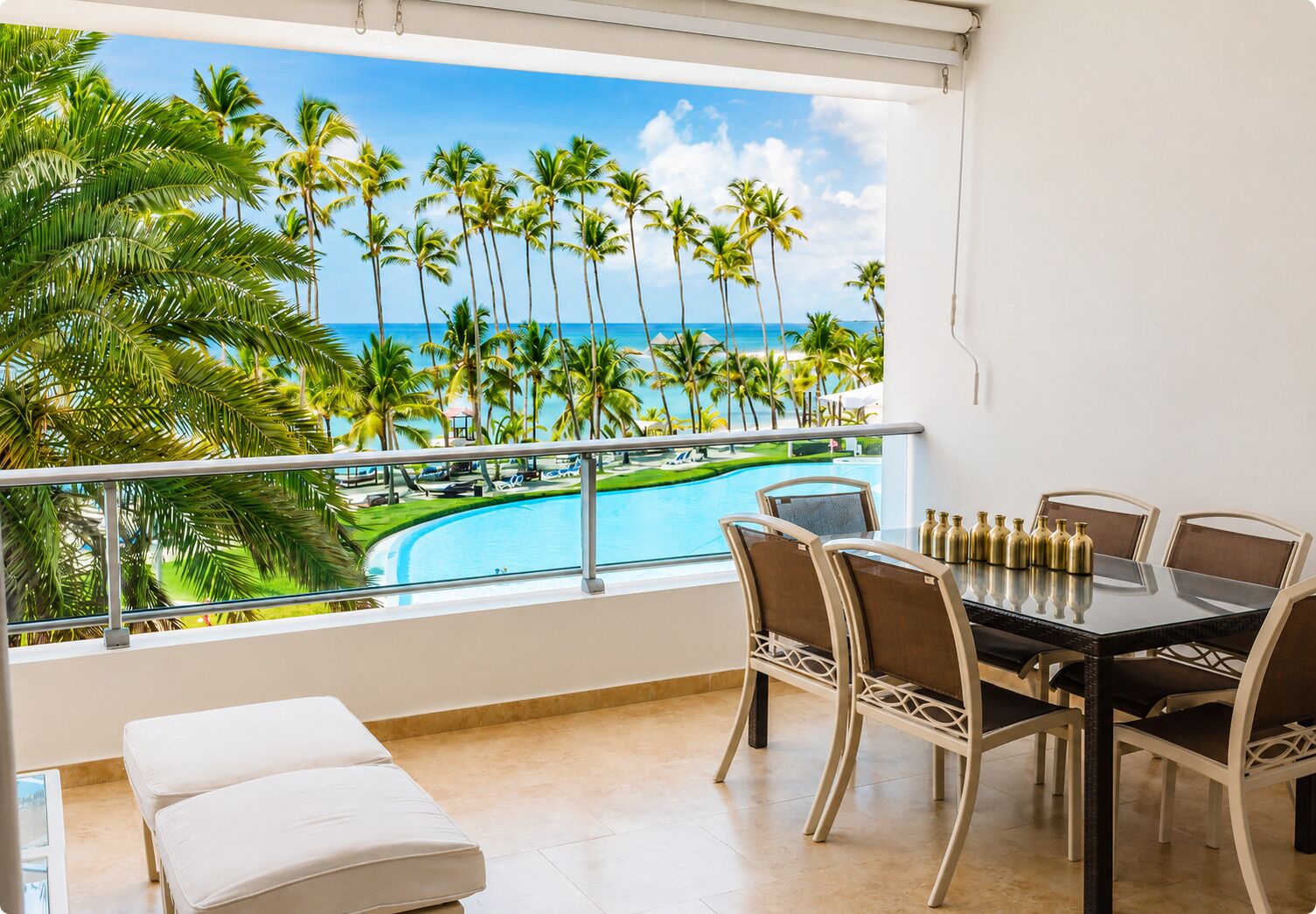 Un balcón con vista a la piscina, una mesa de comedor con sillas y un sofá blanco.