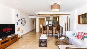 A modern living room with a flat-screen TV, a dining area, and a kitchen.