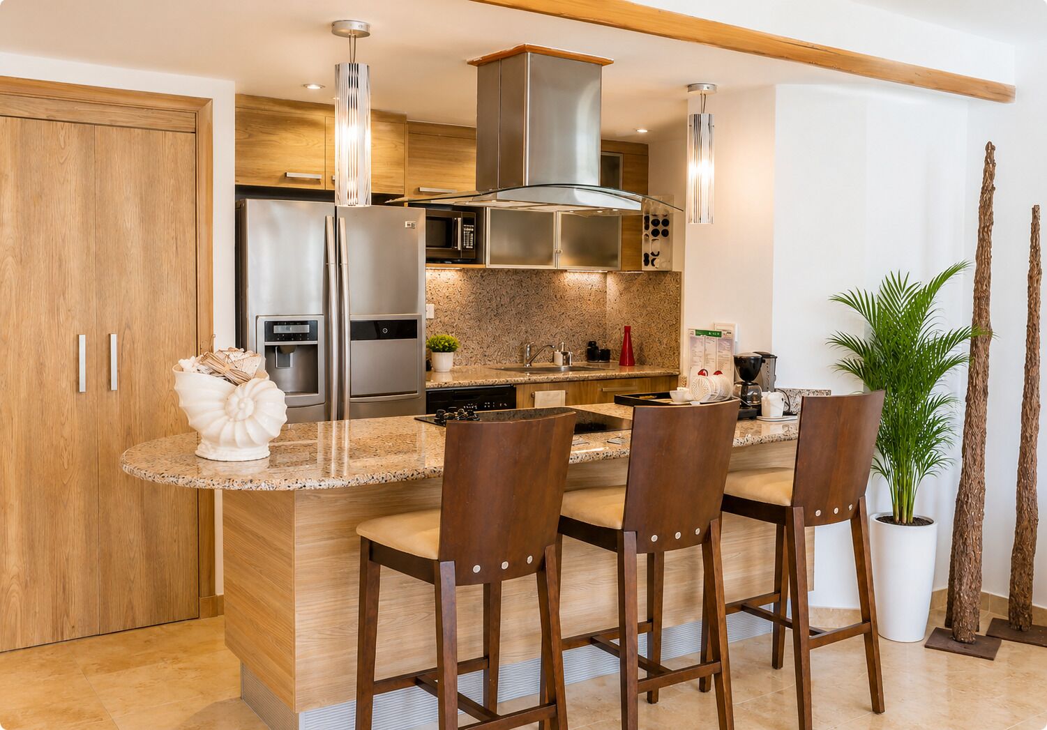 Una cocina moderna con una isla central, taburetes de bar, electrodomésticos de acero inoxidable y un ventanal grande.