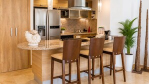 A modern kitchen with a central island, bar stools, stainless steel appliances, and a large window.