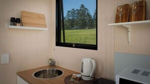 A small kitchenette with a window, a wooden cutting board, a kettle, and a sink. - Tiny Tallowood by Tiny Away (Glenreagh)