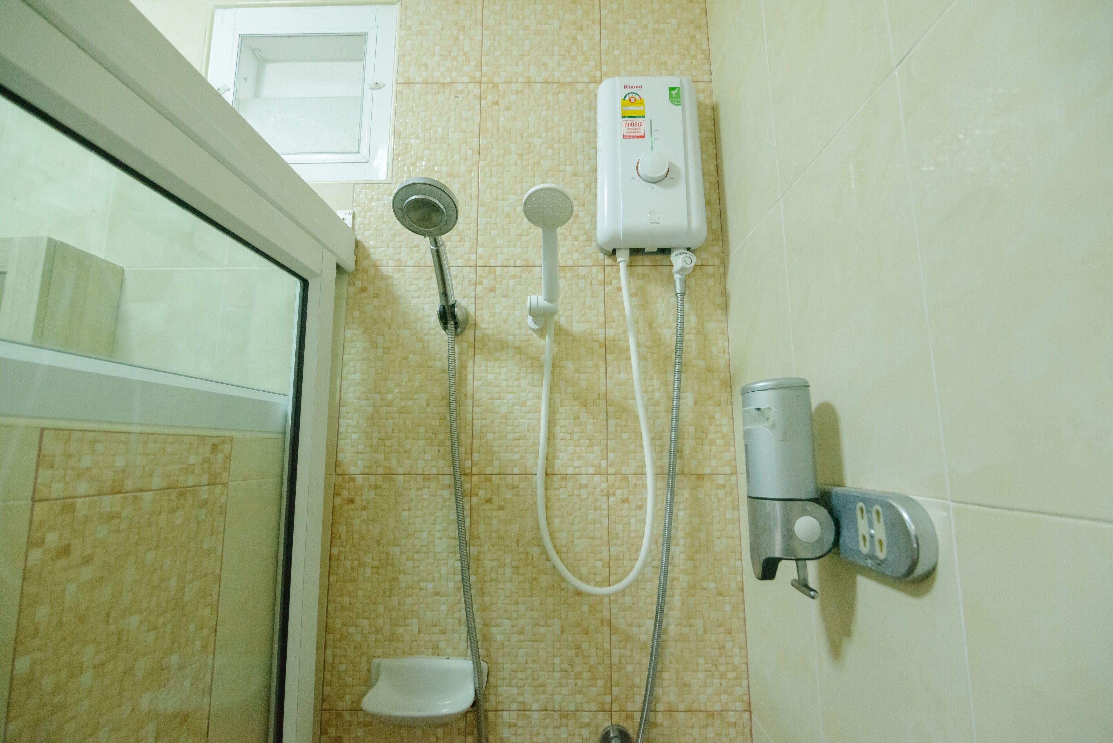 A bathroom with a shower, a handheld showerhead, a wall-mounted faucet, and a soap dispenser.