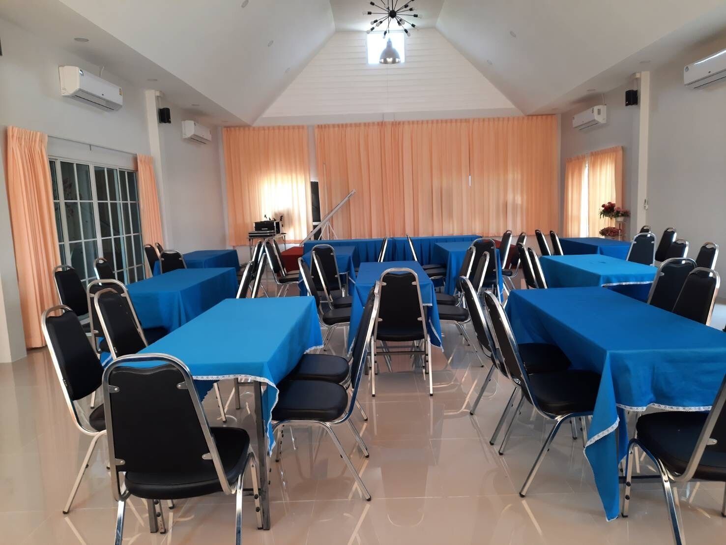 Un salón de conferencias con mesas y sillas, unidades de aire acondicionado y un amplio ventanal con cortinas.