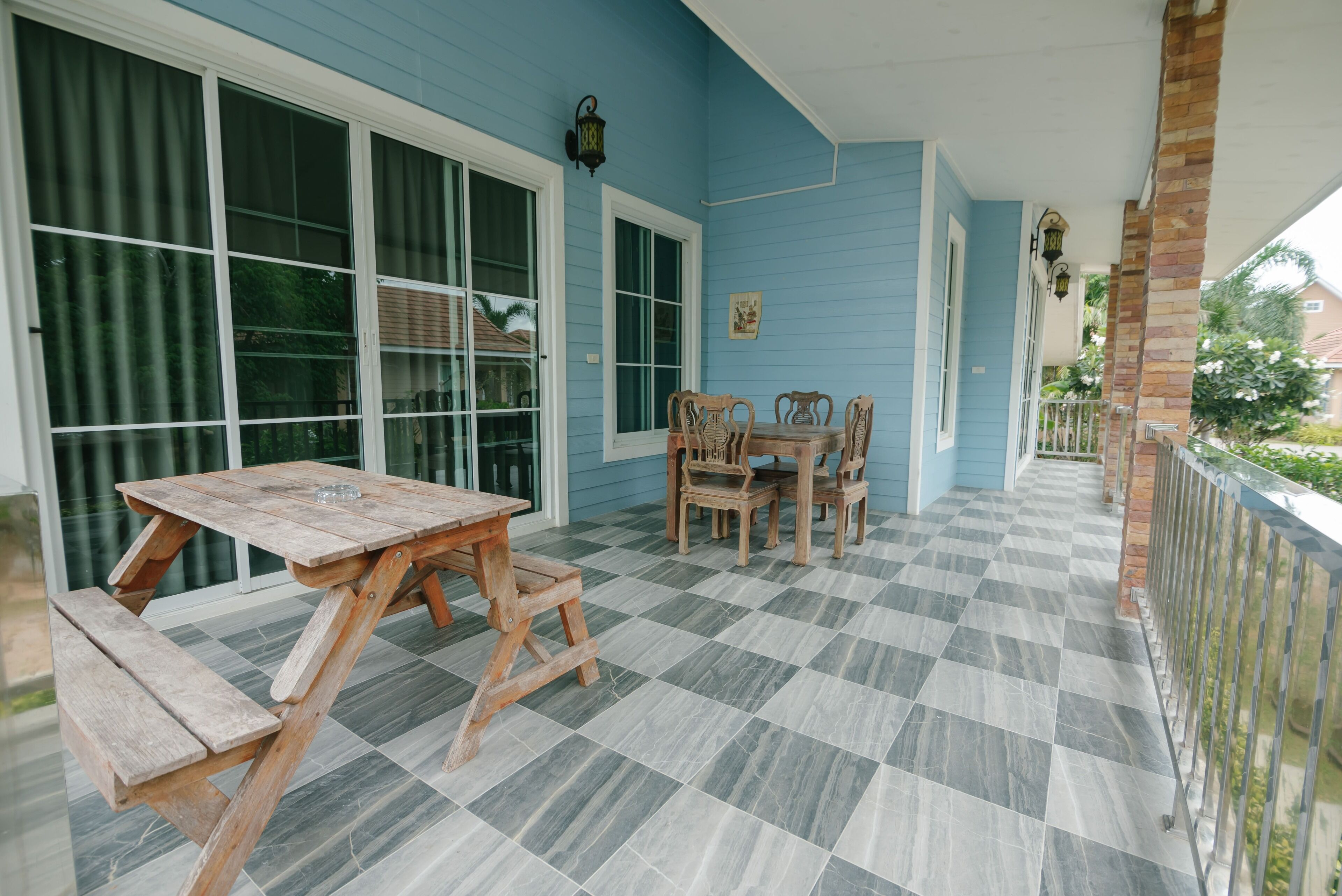 Un patio techado con suelo a cuadros, mobiliario de madera y una pared exterior azul.
