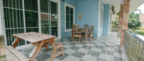 Un patio techado con suelo a cuadros, mobiliario de madera y una pared exterior azul.