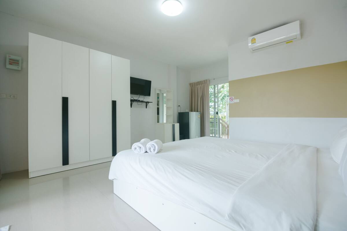 A hotel room with a large bed, a wardrobe, a television, and an air conditioning unit.