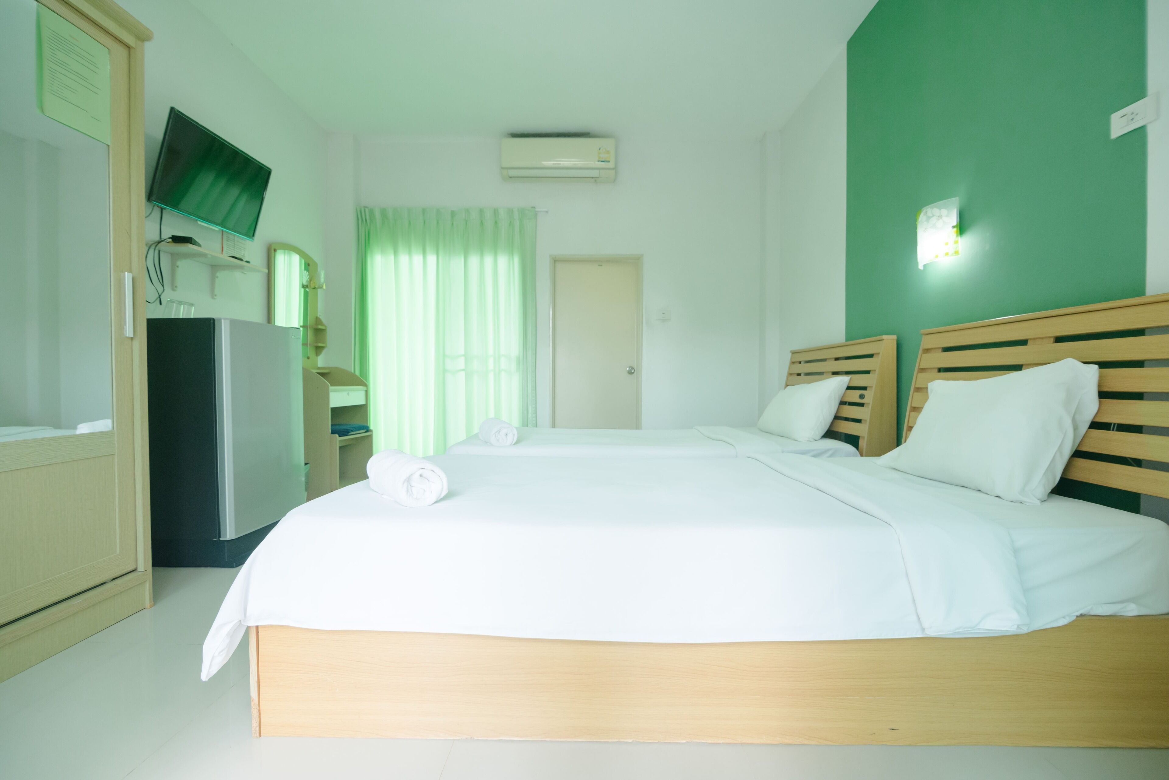 Een hotelkamer met een bed, een televisie, een koelkast en een groene wand.