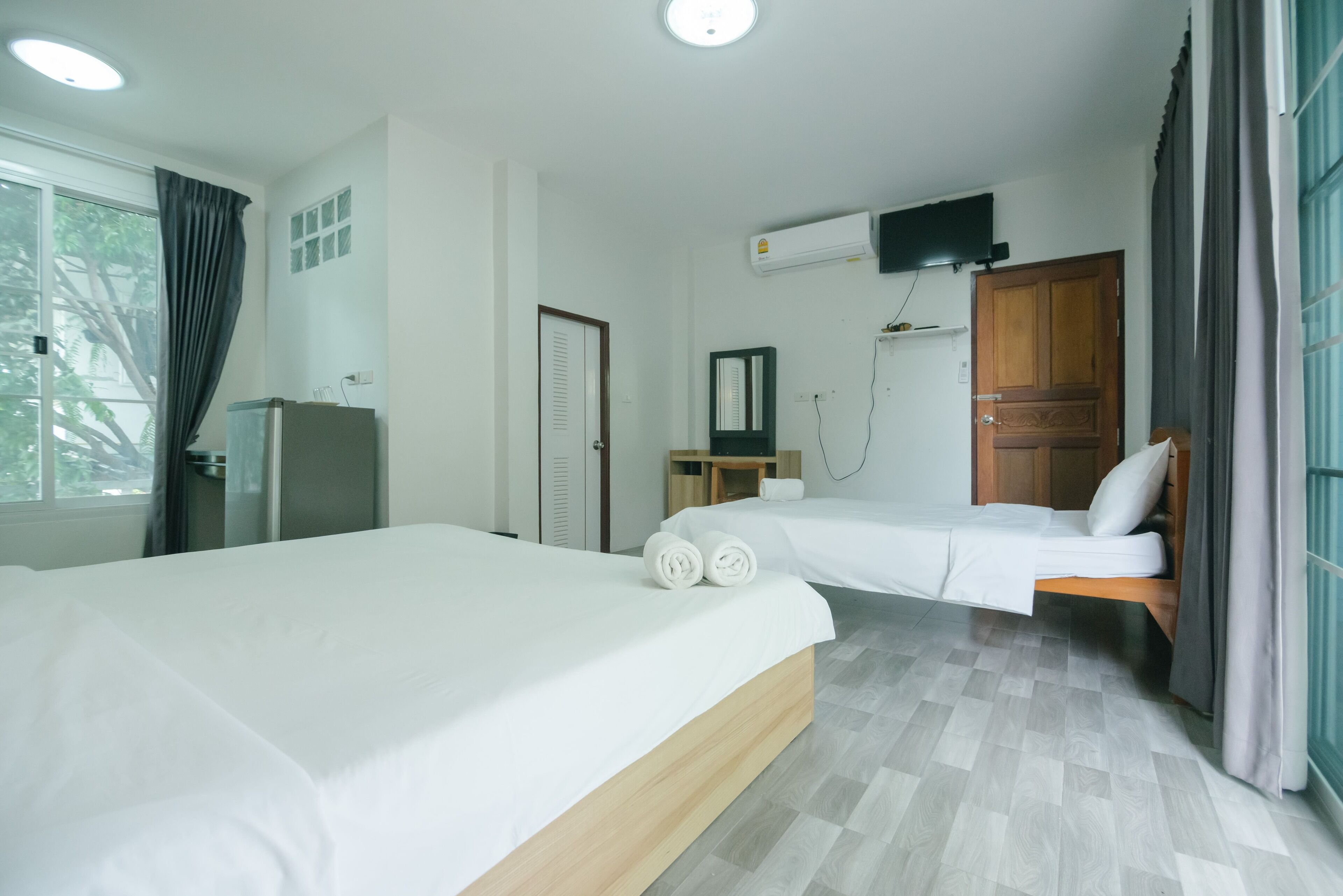 Een hotelkamer met twee bedden, een televisie, een airconditioner en een raam met gordijnen.