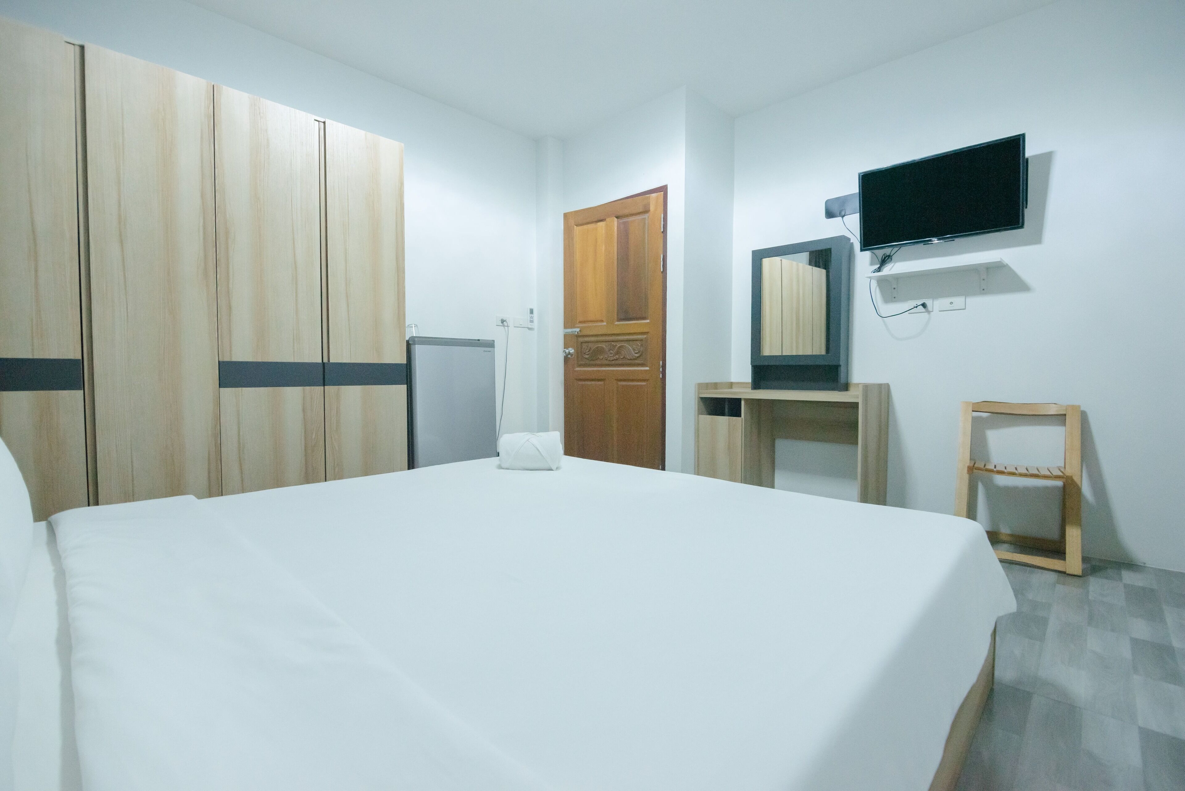 Habitación de hotel con cama, armario, televisor y una pequeña silla de madera.