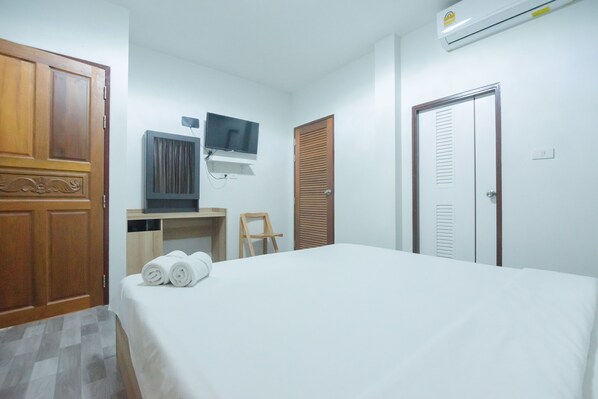 A hotel room with a bed, a desk, a television, a wardrobe, and an air conditioning unit. - Reuan Chom Dao Resort (Chom Bueng)