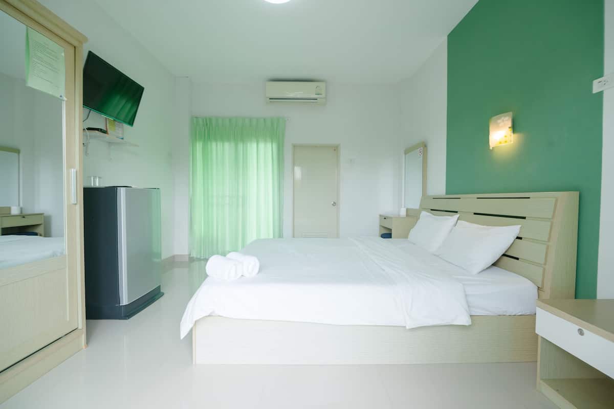 A hotel room with a bed, a TV mounted on the wall, an air conditioner, a desk, and a wardrobe.