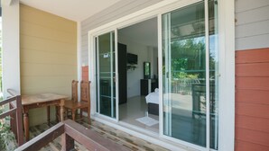 A room with a sliding glass door leading to a balcony, a wooden table, and a chair. - Reuan Chom Dao Resort (Chom Bueng)