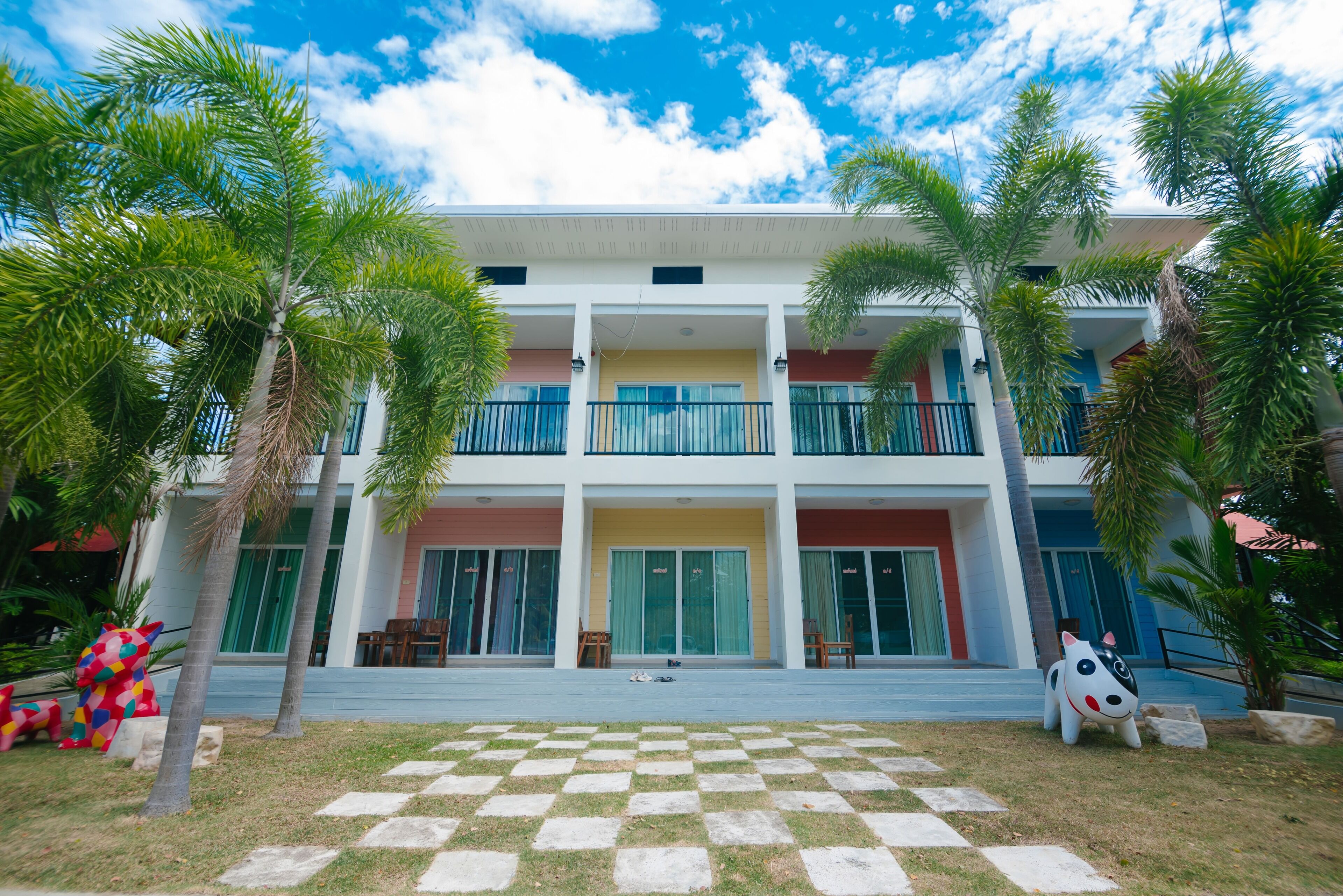 A two-story building with a checkered lawn in front, palm trees, and a colorful sculpture.