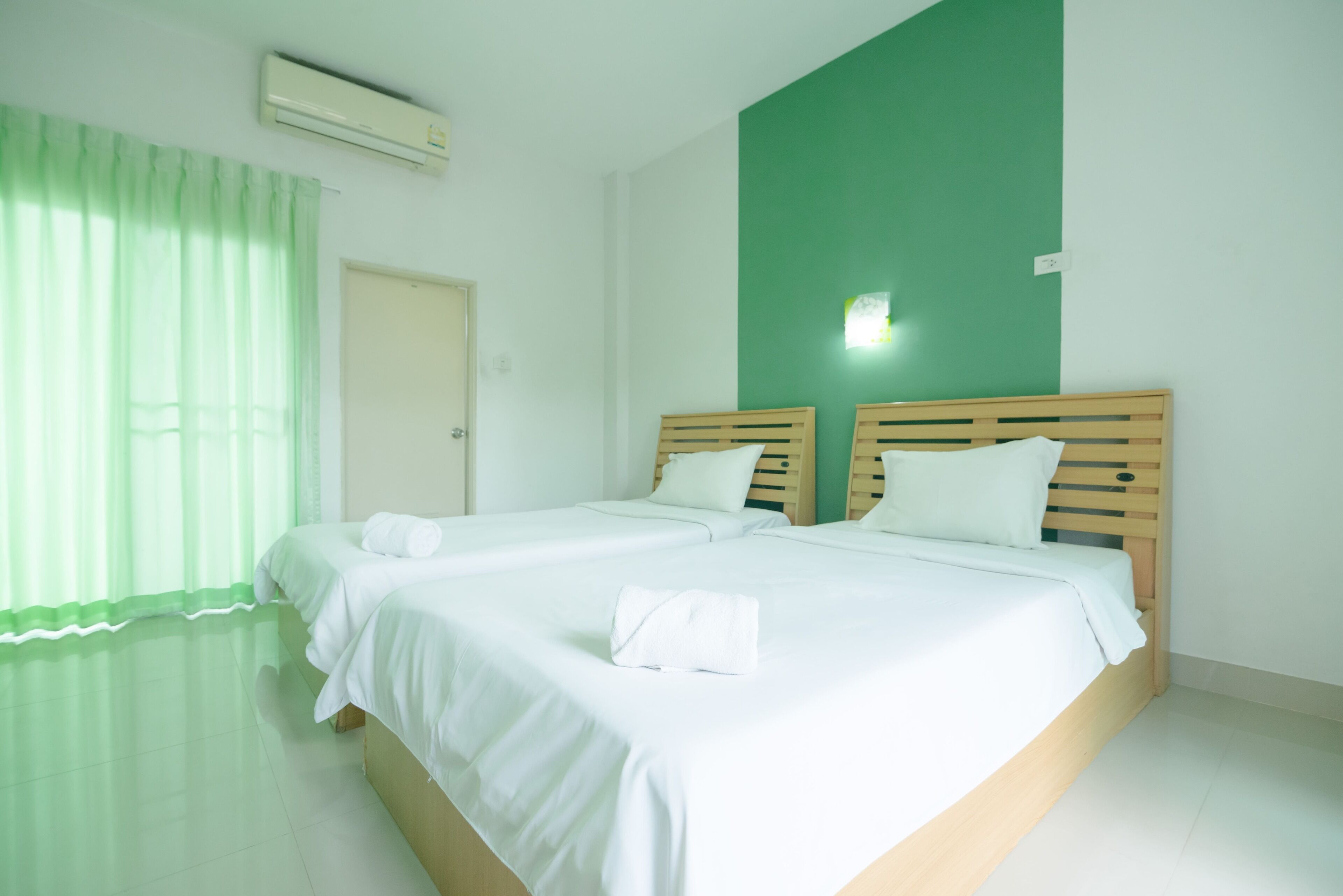 Una habitación de hotel limpia y moderna con dos camas, una pared de acento verde y un ambiente luminoso y bien iluminado.