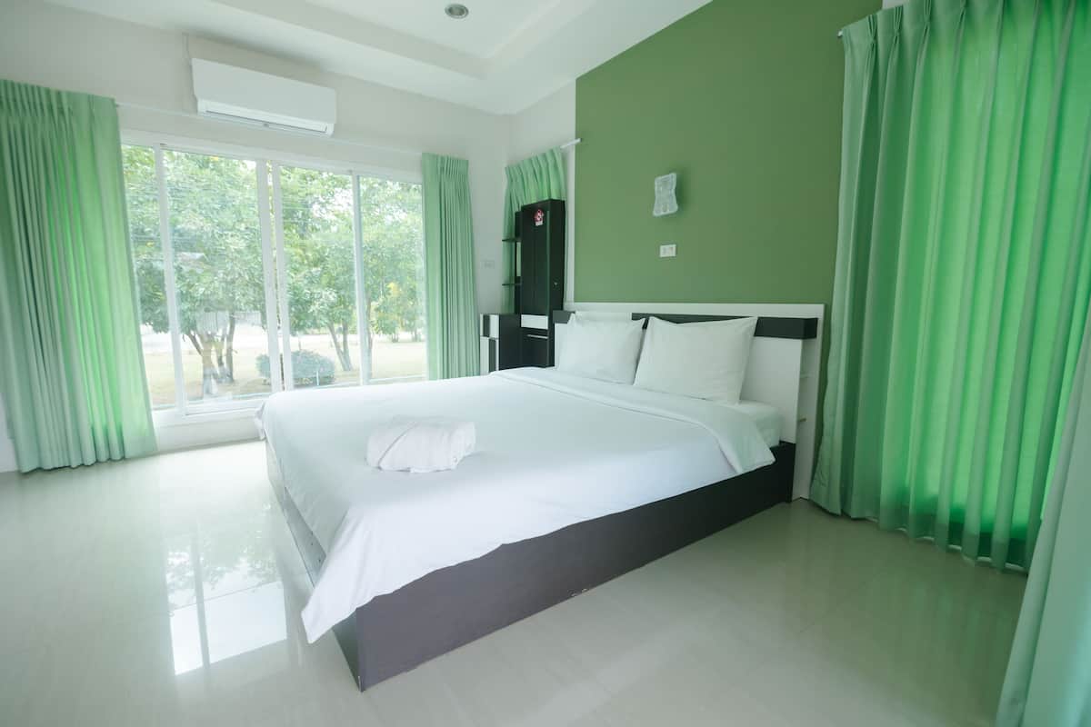 A hotel room with a large bed, green curtains, and a view of the outdoors.