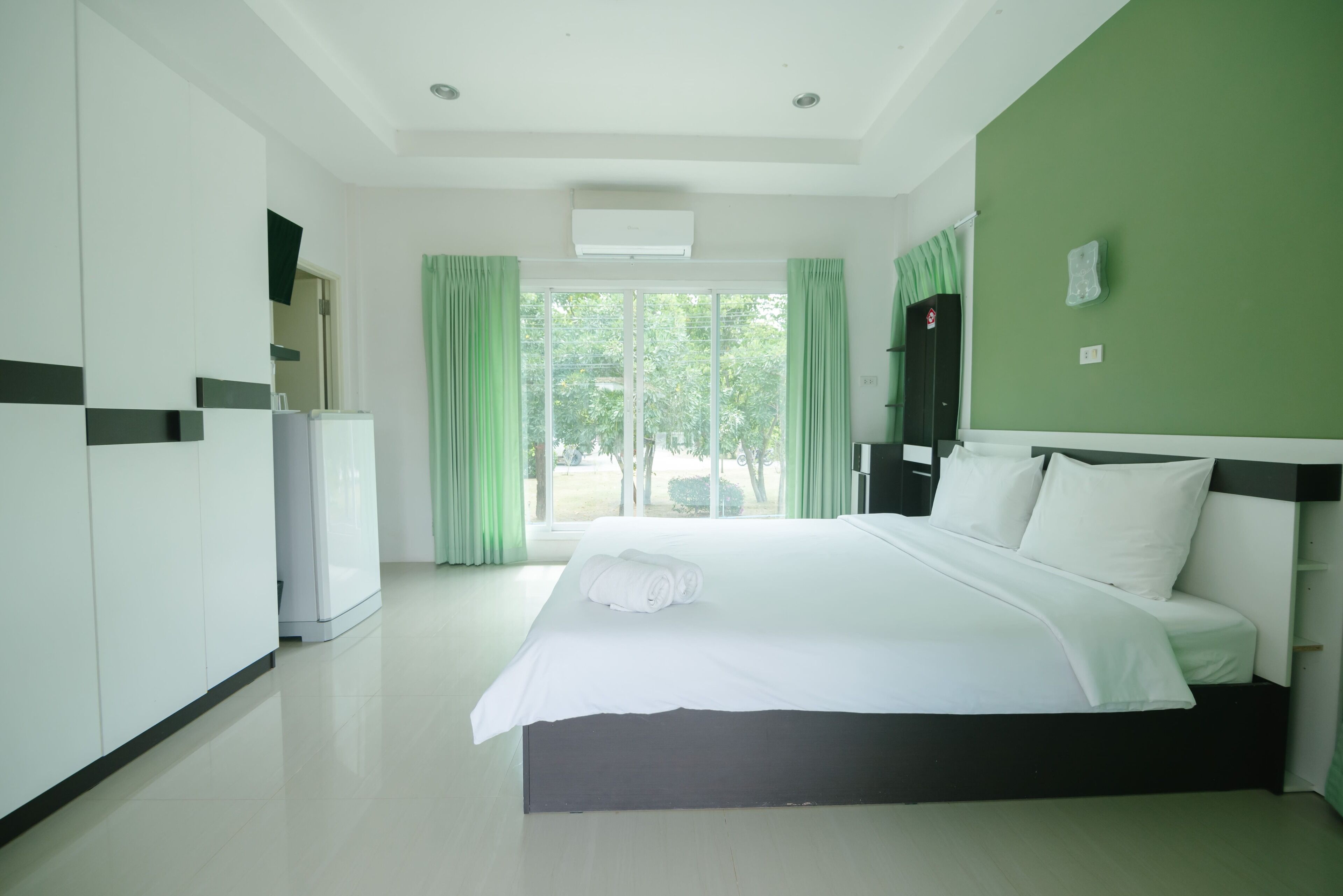 A hotel room with a large bed, a wardrobe, a desk, and a window with curtains.