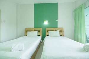 Una habitación de hotel con dos camas individuales, una pared de acento verde y una ventana con cortinas.