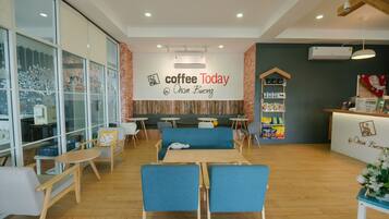 A modern coffee shop interior with seating, a counter, and a wall with the text "coffee Today @ Cham Bueng".