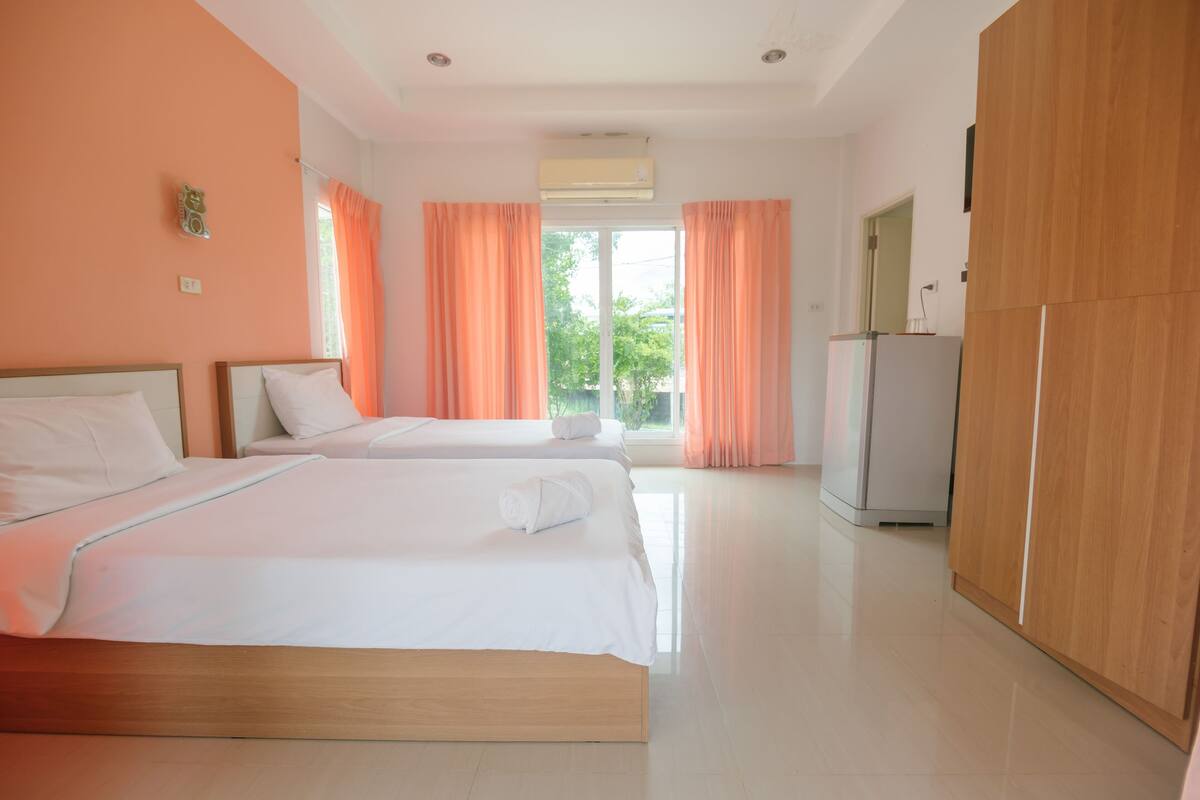 A hotel room with two beds, an air conditioner, a wardrobe, and a window with curtains.